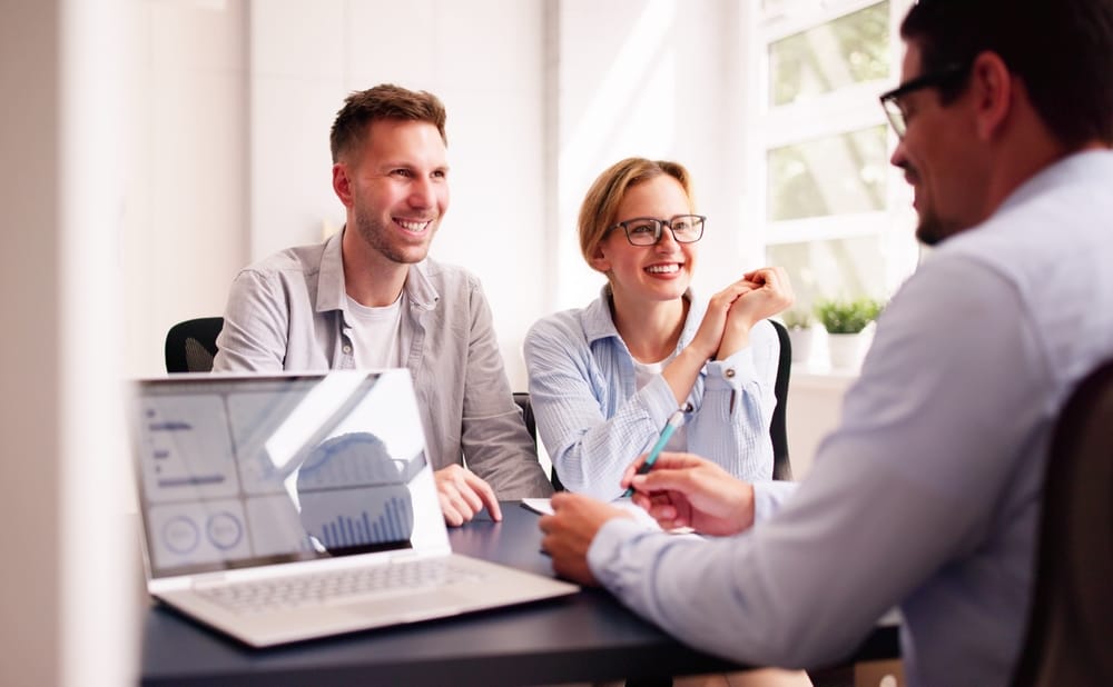 Young couple discussing their financial future with a financial accountant and financial planner in the office, using a laptop and notebook.