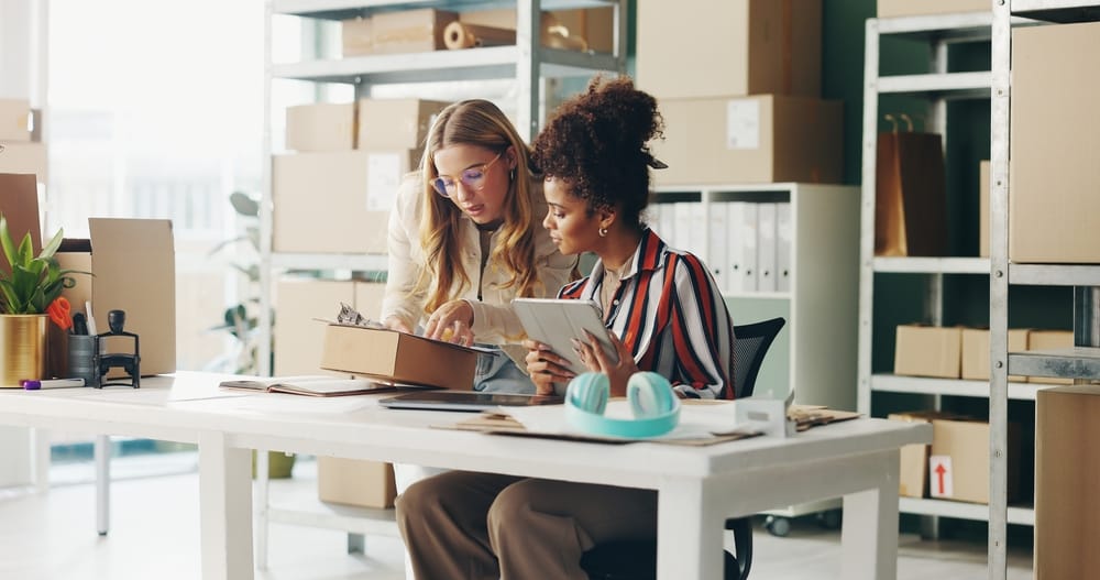 Women, tablet and teamwork for office logistics, package and e commerce checklist with stock of online shop. Small business people or seller with digital tech, box and clipboard for website order